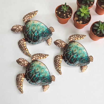 Three teal sea turtle wall sculptures displayed next to small succulent plants
